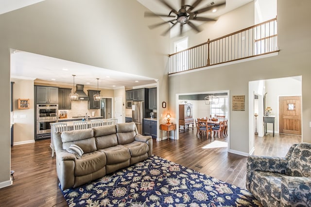 living room featuring ornamental molding, a high ceiling, dark wood-type flooring, and ceiling fan