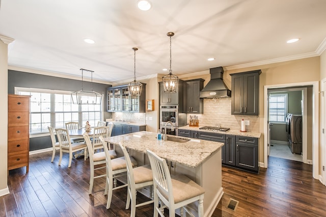 kitchen featuring washer / clothes dryer, decorative light fixtures, dark wood-type flooring, premium range hood, and a kitchen island with sink