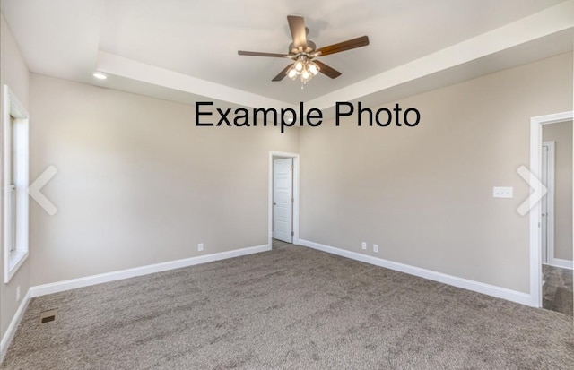 carpeted empty room with a raised ceiling and ceiling fan