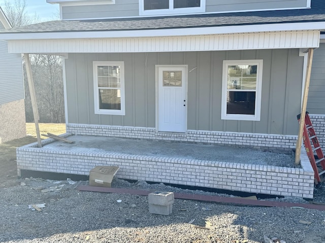 doorway to property with covered porch and roof with shingles