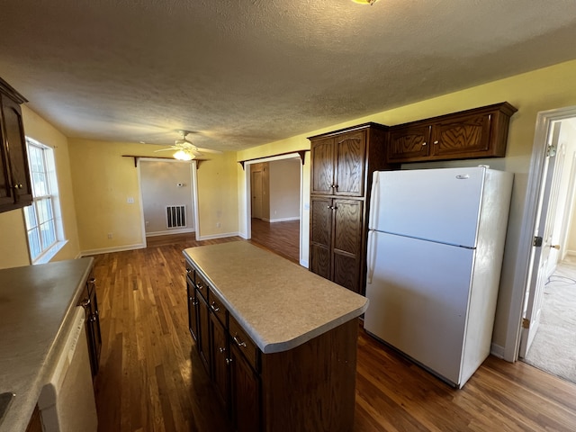 kitchen with ceiling fan, dark wood-type flooring, dark brown cabinetry, a center island, and white appliances