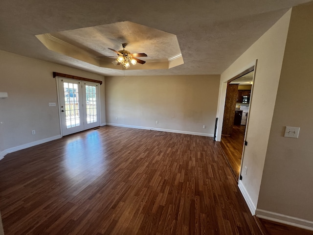 unfurnished room featuring french doors, dark wood-type flooring, a tray ceiling, ornamental molding, and ceiling fan