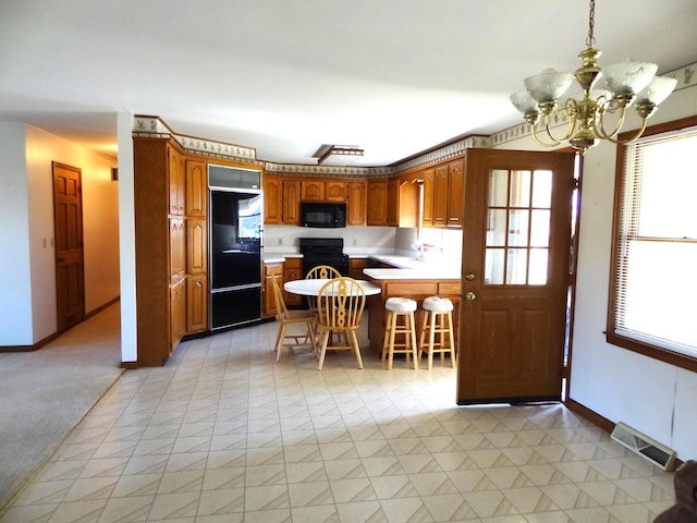 kitchen featuring kitchen peninsula, black appliances, a breakfast bar, a notable chandelier, and pendant lighting