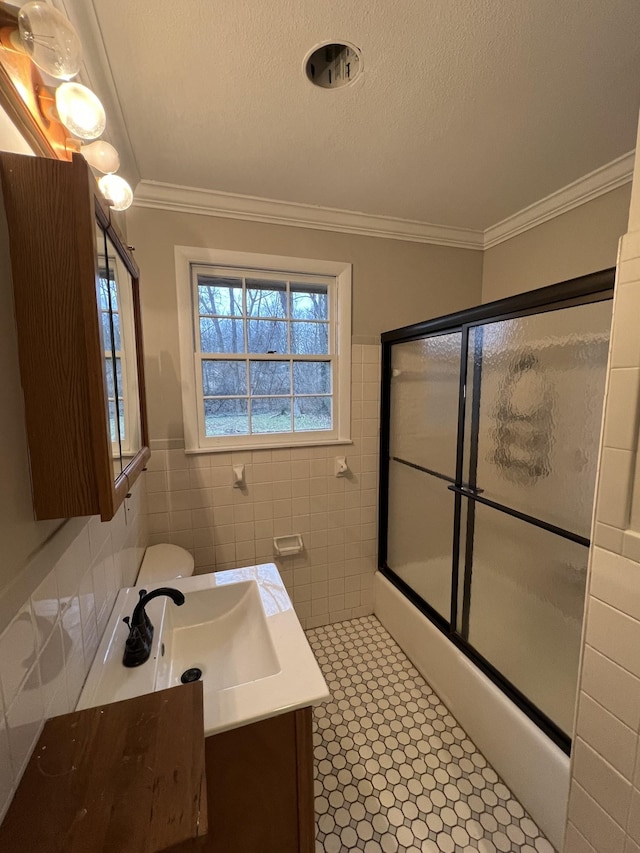 full bathroom featuring ornamental molding, combined bath / shower with glass door, tile walls, and a textured ceiling