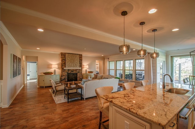 kitchen with sink, dark hardwood / wood-style flooring, decorative light fixtures, crown molding, and a kitchen island with sink