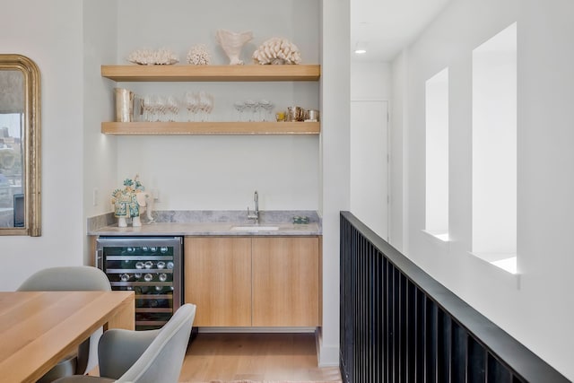 bar with light brown cabinets, sink, wine cooler, and light hardwood / wood-style flooring