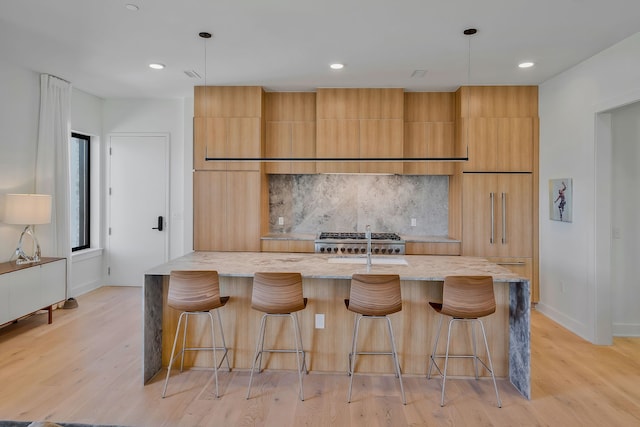 kitchen featuring a kitchen bar, pendant lighting, light hardwood / wood-style flooring, and a kitchen island with sink