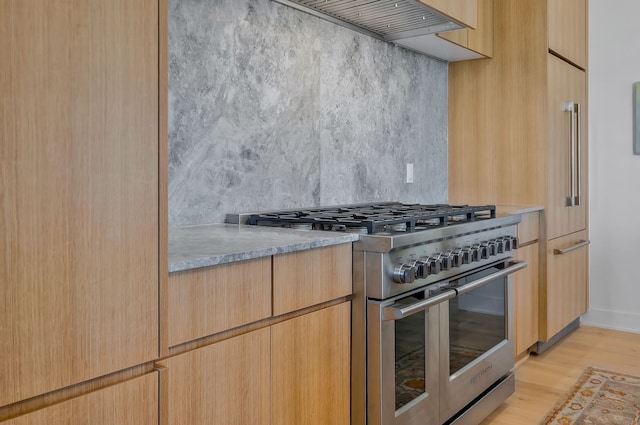 kitchen with tasteful backsplash, light brown cabinetry, high end stainless steel range oven, and light wood-type flooring