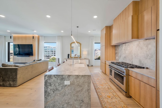 kitchen with a center island with sink, range with two ovens, sink, decorative backsplash, and decorative light fixtures