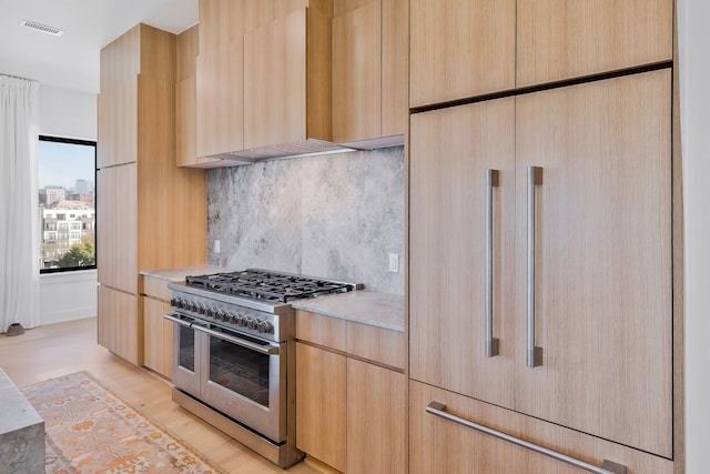 kitchen featuring light brown cabinets, double oven range, fridge, and wall chimney range hood