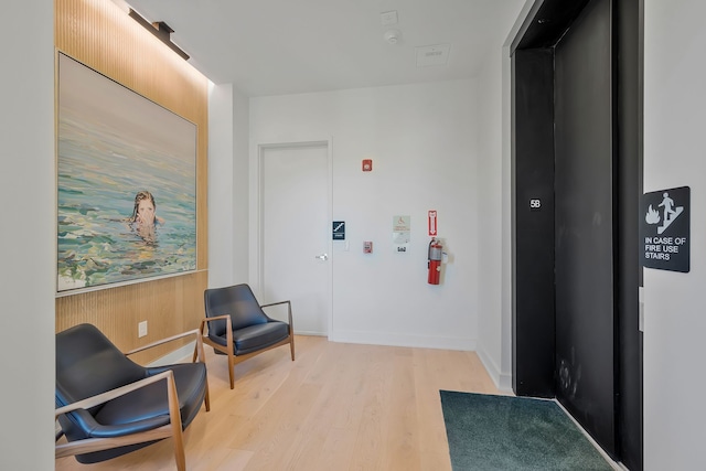 hall with light wood-type flooring, elevator, and wood walls