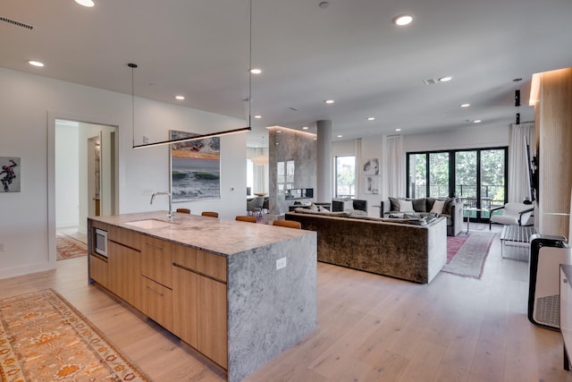 kitchen with light wood-type flooring, light stone counters, a spacious island, and sink