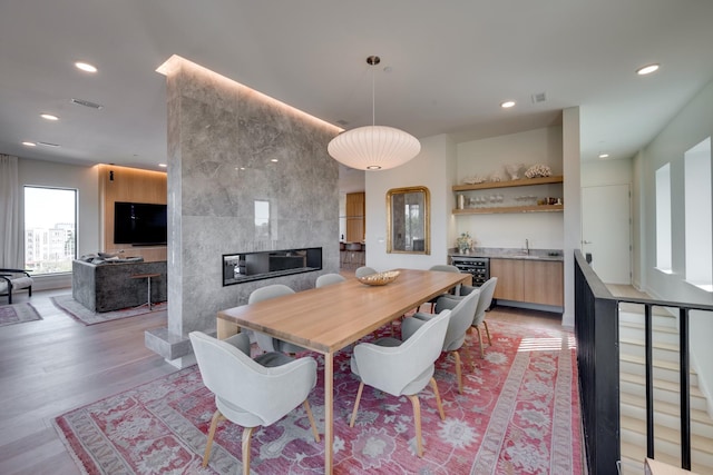 dining space with a fireplace, light wood-type flooring, and indoor bar