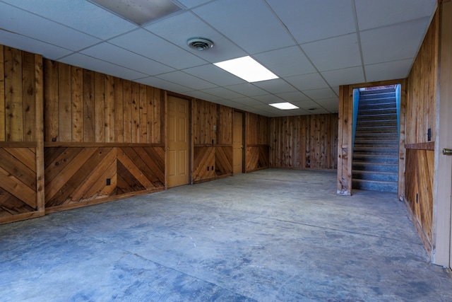 basement featuring a drop ceiling and wood walls