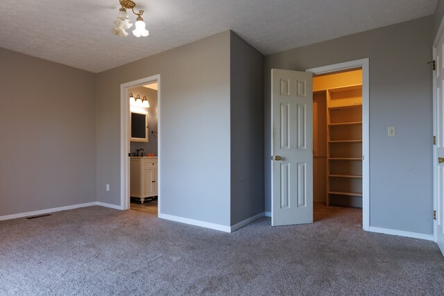 unfurnished bedroom featuring a walk in closet, ensuite bath, a textured ceiling, carpet floors, and a closet