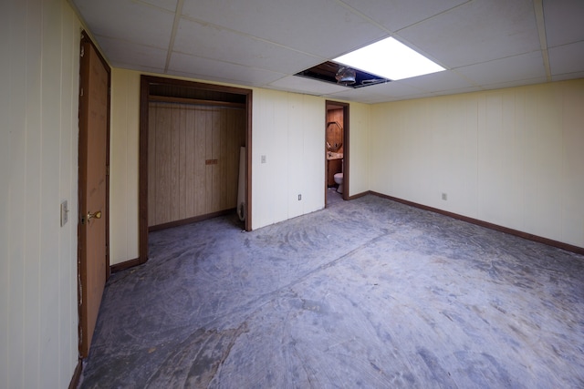 unfurnished bedroom featuring connected bathroom, a drop ceiling, a closet, and wooden walls