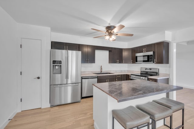 kitchen featuring sink, stainless steel appliances, a kitchen breakfast bar, light hardwood / wood-style flooring, and dark brown cabinets