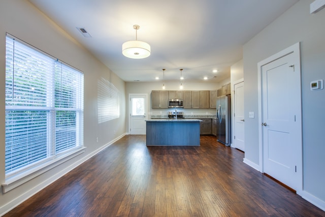 kitchen with appliances with stainless steel finishes, decorative light fixtures, a center island with sink, and dark hardwood / wood-style flooring