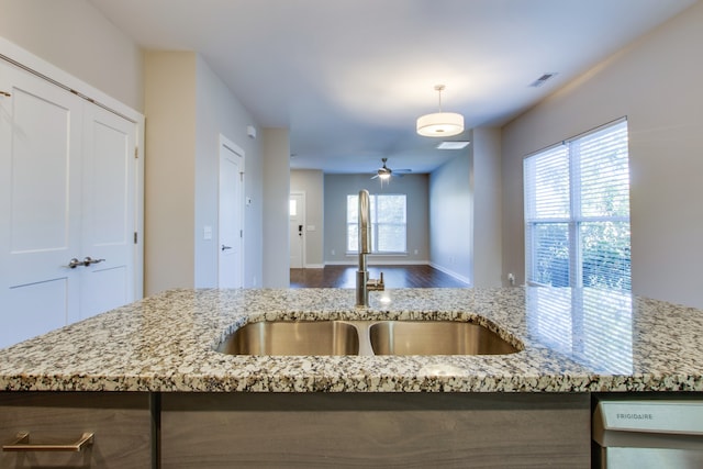 kitchen with sink, hardwood / wood-style floors, ceiling fan, decorative light fixtures, and light stone counters