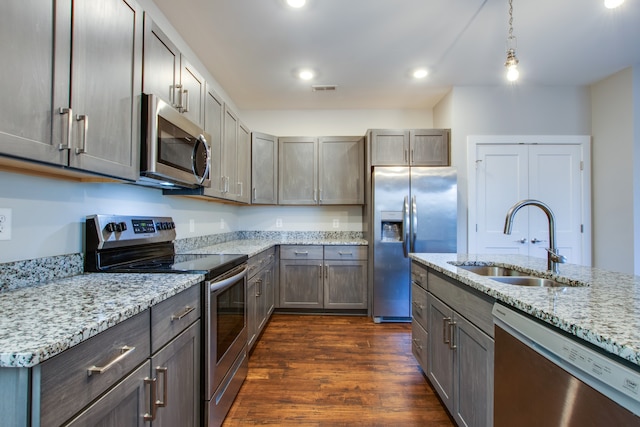 kitchen featuring sink, hanging light fixtures, stainless steel appliances, light stone counters, and dark hardwood / wood-style floors