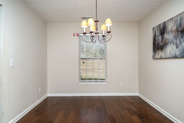 unfurnished dining area with a textured ceiling, an inviting chandelier, and dark hardwood / wood-style flooring