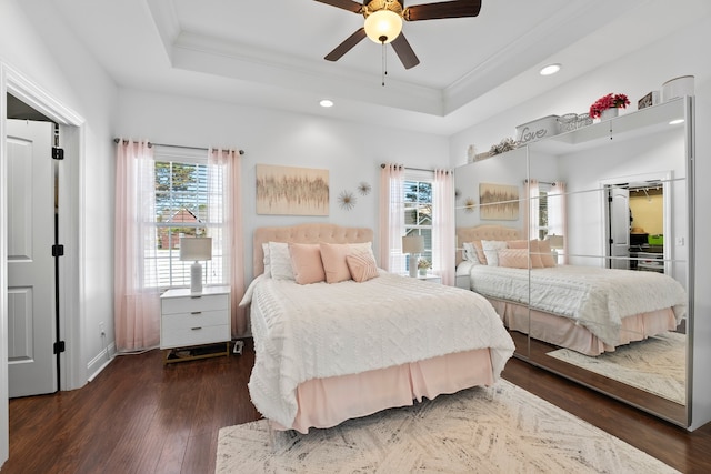 bedroom featuring ornamental molding, dark wood-type flooring, a tray ceiling, and ceiling fan