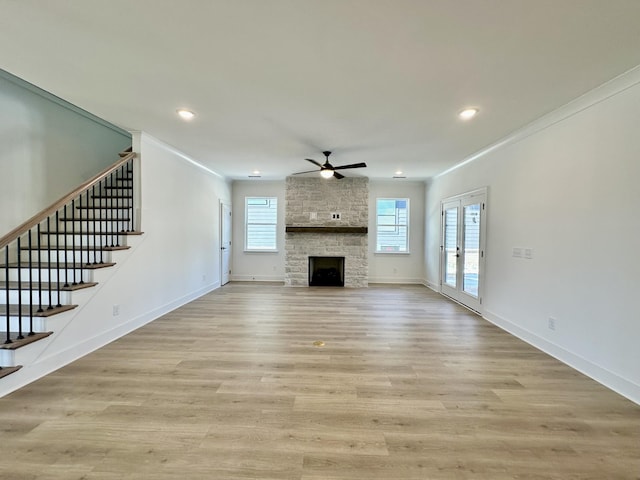 unfurnished living room featuring a fireplace, crown molding, light wood-type flooring, baseboards, and stairs