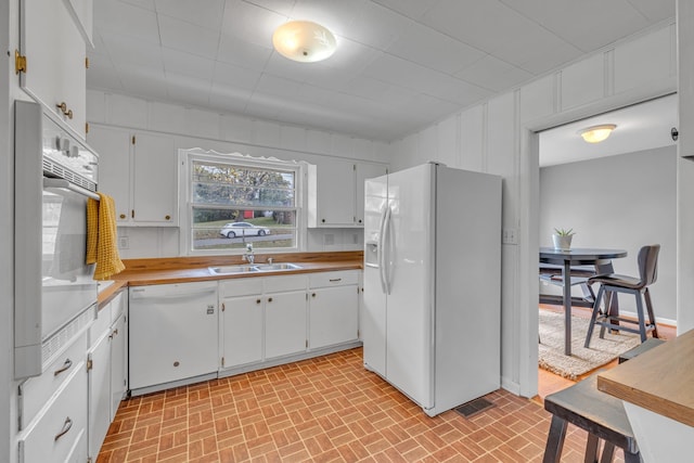 kitchen featuring white appliances, white cabinetry, sink, and wooden walls