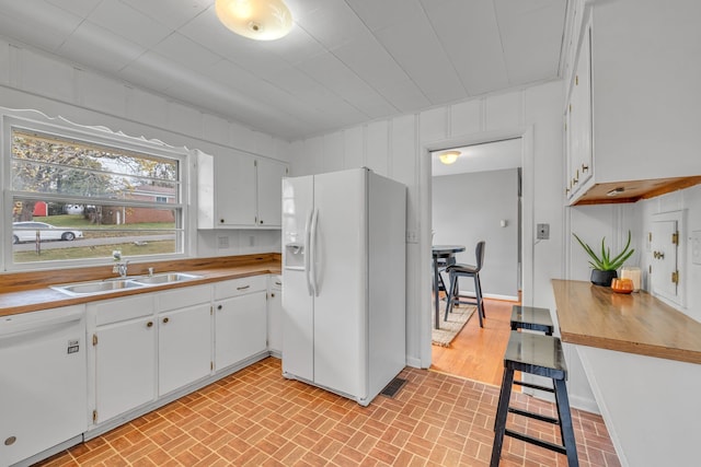 kitchen with sink, white cabinetry, white appliances, and wood walls