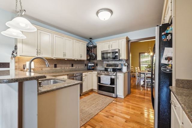 kitchen with kitchen peninsula, appliances with stainless steel finishes, light hardwood / wood-style flooring, pendant lighting, and sink