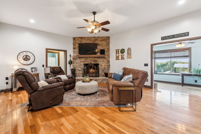 living room with ceiling fan, a stone fireplace, and light hardwood / wood-style flooring