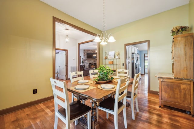 dining area with a notable chandelier, a stone fireplace, and dark hardwood / wood-style flooring