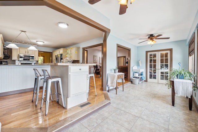 kitchen with appliances with stainless steel finishes, french doors, a breakfast bar area, ceiling fan, and light hardwood / wood-style flooring