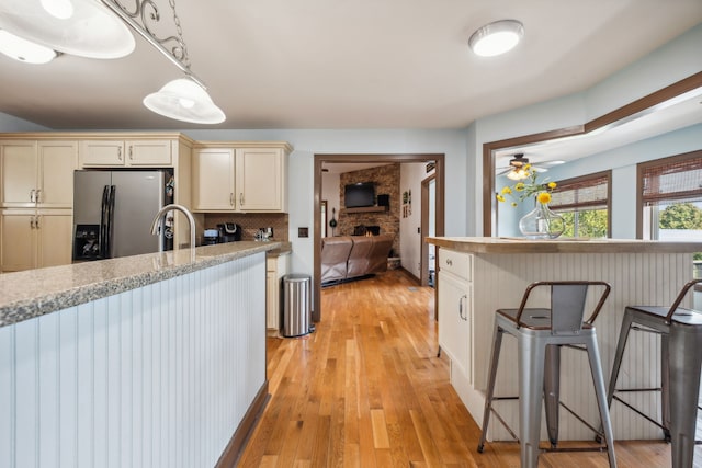 kitchen featuring stainless steel fridge, hanging light fixtures, light wood-type flooring, cream cabinetry, and light stone counters