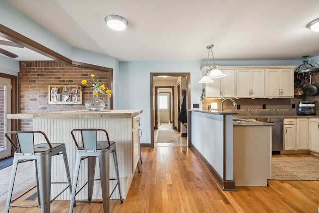 kitchen with dishwasher, light wood-type flooring, a kitchen bar, pendant lighting, and decorative backsplash