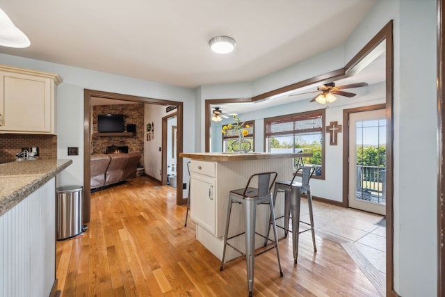 kitchen with light wood-type flooring, a large fireplace, backsplash, ceiling fan, and a breakfast bar area