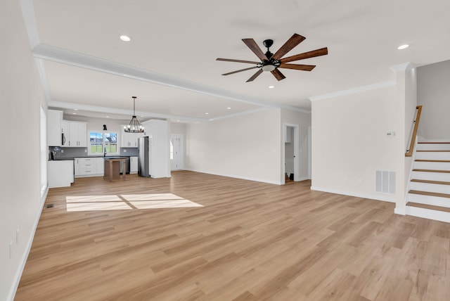 unfurnished living room with ornamental molding, ceiling fan with notable chandelier, and light wood-type flooring