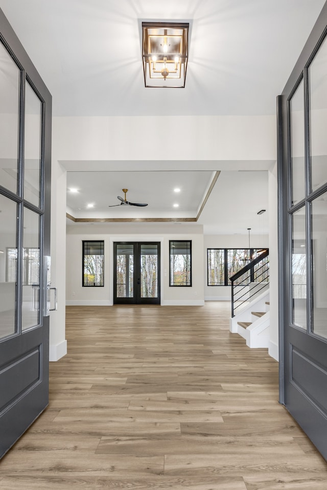 foyer entrance featuring french doors, a tray ceiling, light hardwood / wood-style flooring, and ceiling fan