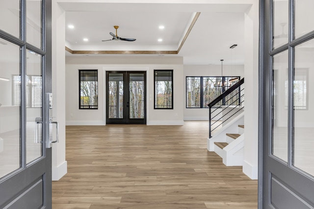 foyer featuring ceiling fan with notable chandelier, french doors, a tray ceiling, and light hardwood / wood-style flooring