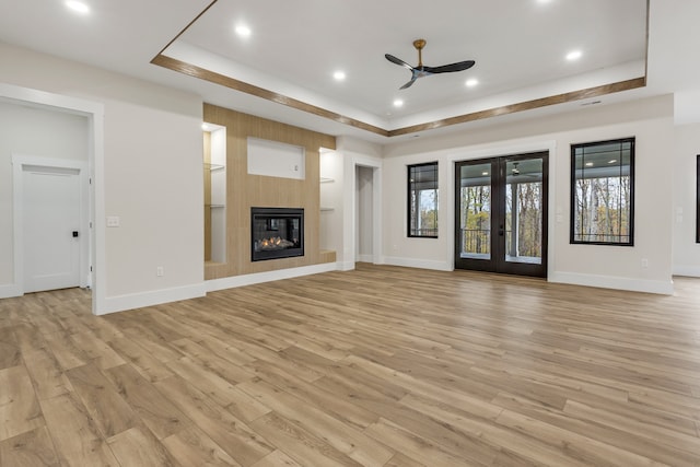 unfurnished living room featuring a fireplace, french doors, light wood-type flooring, and ceiling fan