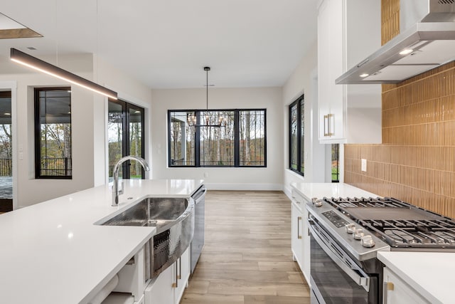 kitchen with pendant lighting, backsplash, white cabinets, wall chimney exhaust hood, and appliances with stainless steel finishes