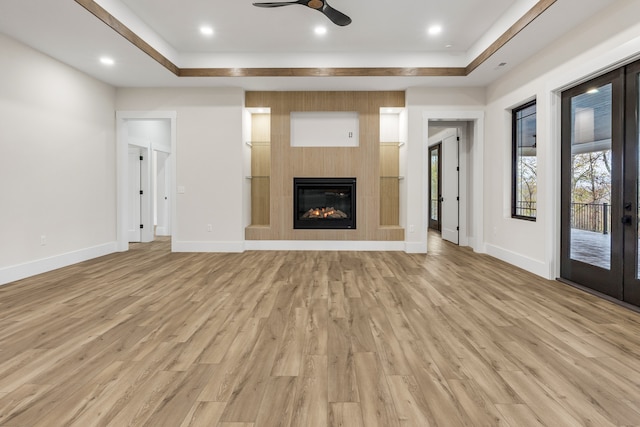 unfurnished living room featuring a raised ceiling, ceiling fan, a fireplace, and light hardwood / wood-style floors