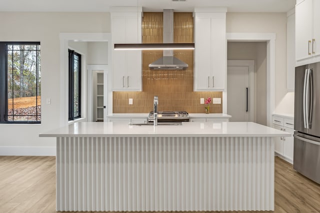 kitchen with tasteful backsplash, stainless steel refrigerator, a kitchen island with sink, and white cabinetry