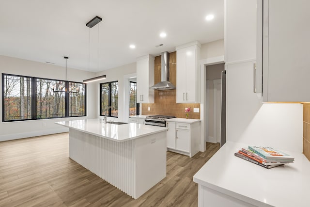 kitchen with wall chimney exhaust hood, stainless steel gas range oven, decorative light fixtures, white cabinets, and light wood-type flooring