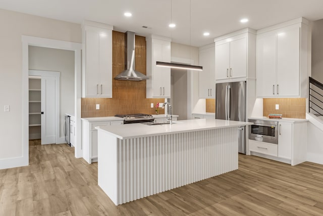 kitchen featuring wall chimney exhaust hood, white cabinetry, a kitchen island with sink, and stainless steel appliances