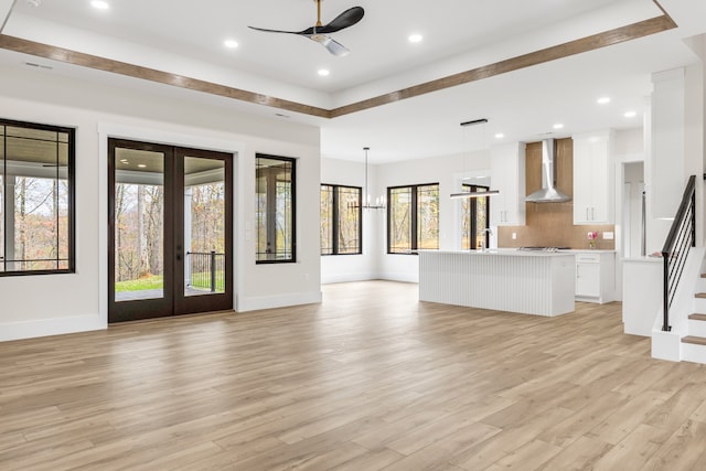 unfurnished living room featuring ceiling fan with notable chandelier, a healthy amount of sunlight, light wood-type flooring, and french doors