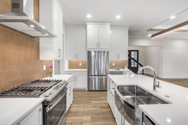 kitchen featuring appliances with stainless steel finishes, sink, wall chimney range hood, light hardwood / wood-style floors, and white cabinetry