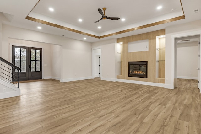 unfurnished living room featuring french doors, a raised ceiling, light hardwood / wood-style flooring, and ceiling fan