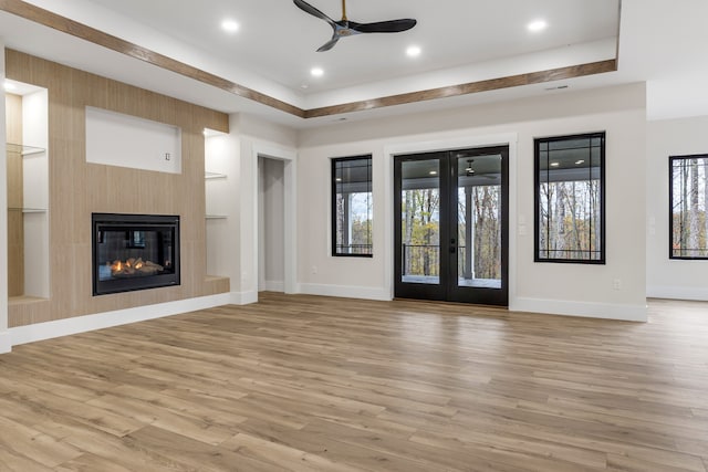 unfurnished living room with ceiling fan, a large fireplace, french doors, and light wood-type flooring