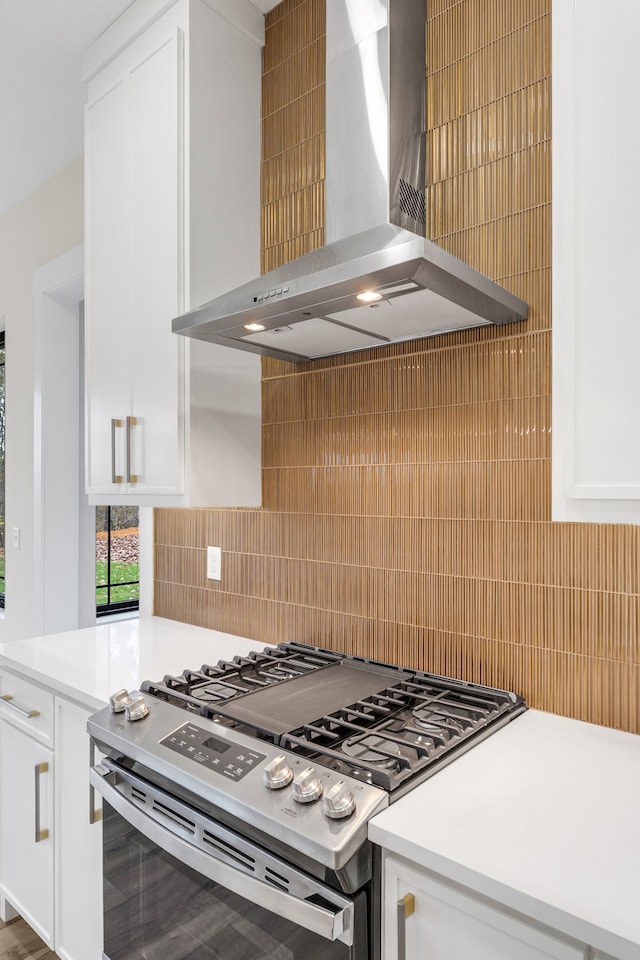 kitchen with white cabinets, gas stove, backsplash, and wall chimney range hood